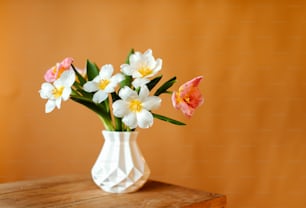 Un jarrón blanco lleno de flores encima de una mesa de madera