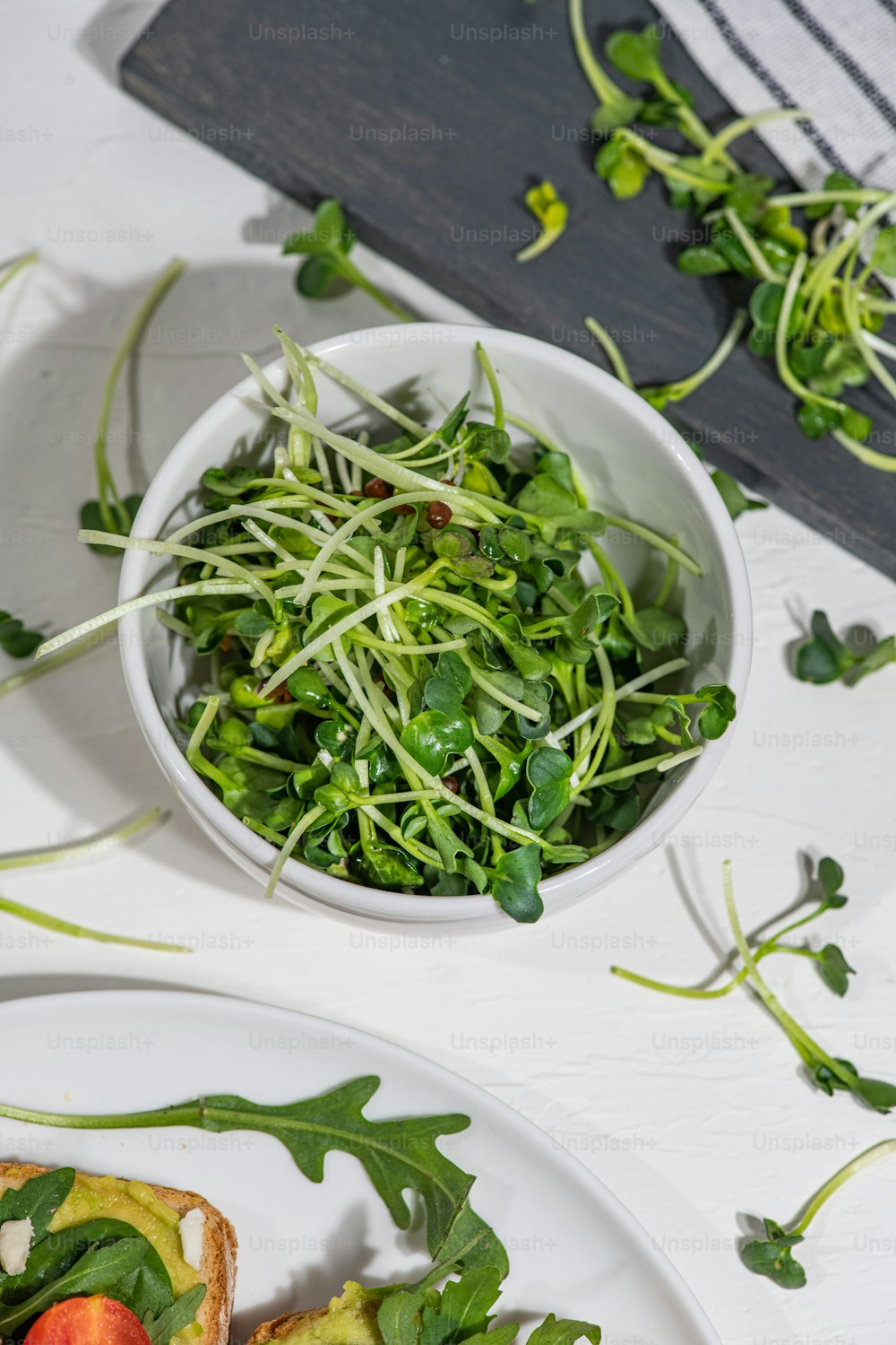 a white plate topped with a salad next to a bowl of greens