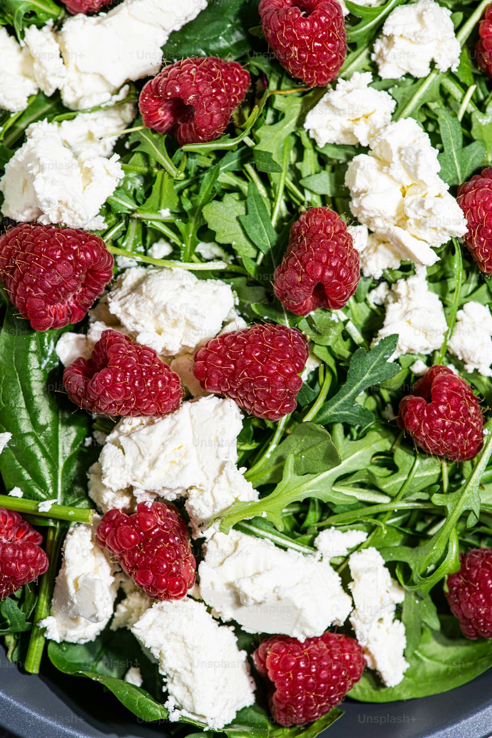 a bowl filled with spinach, cheese and raspberries