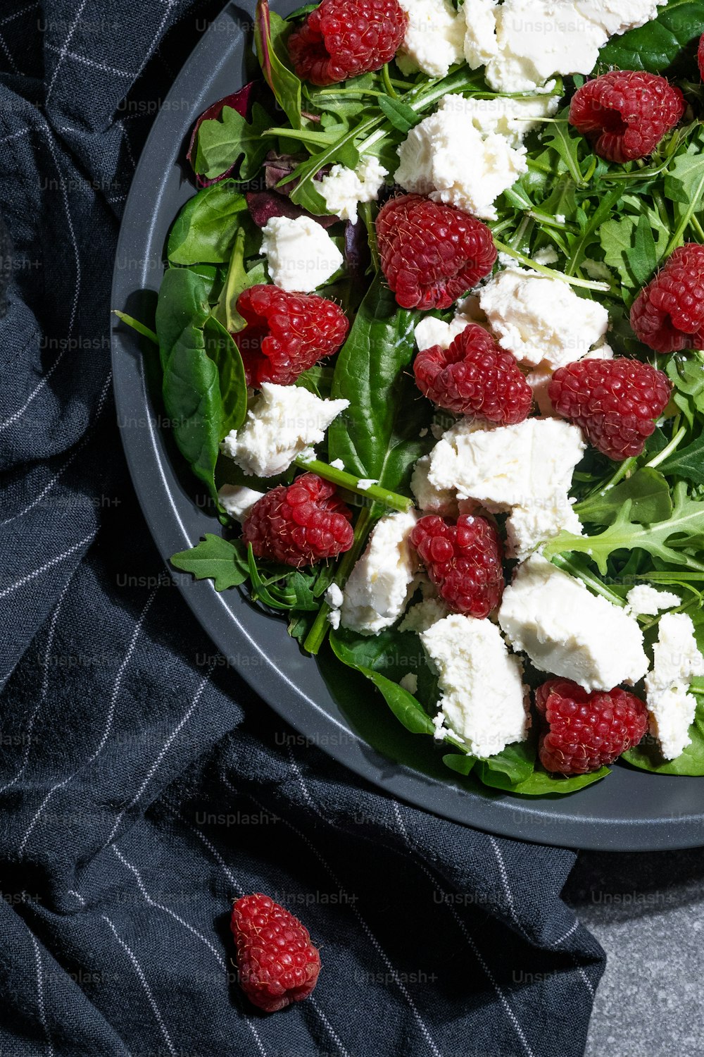 a plate of salad with raspberries and feta cheese