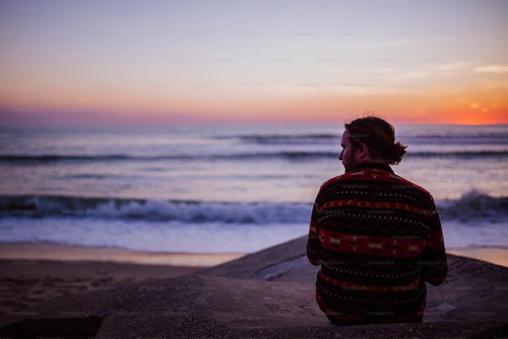 um homem sentado em uma rocha olhando para o oceano
