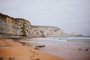 uma praia de areia ao lado de um penhasco e um corpo de água
