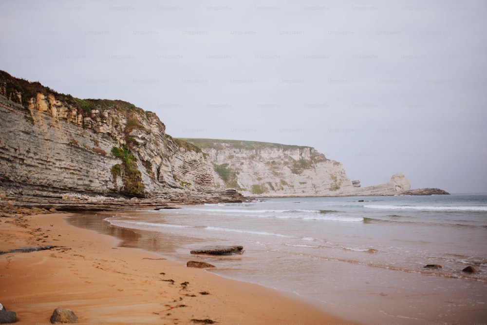 a sandy beach next to a cliff and a body of water