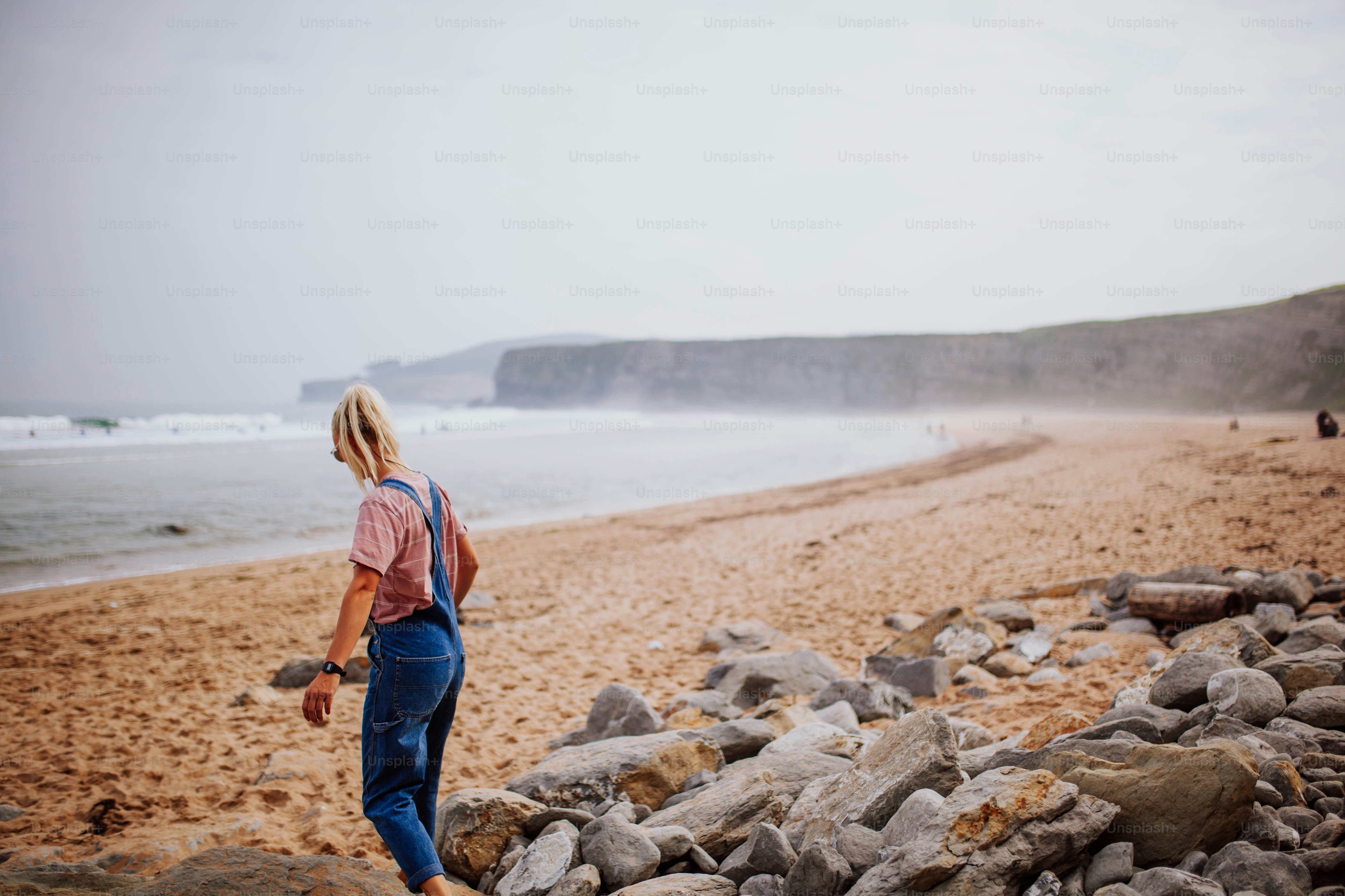 A woman standing on top of a rocky beach next to the ocean photo ...