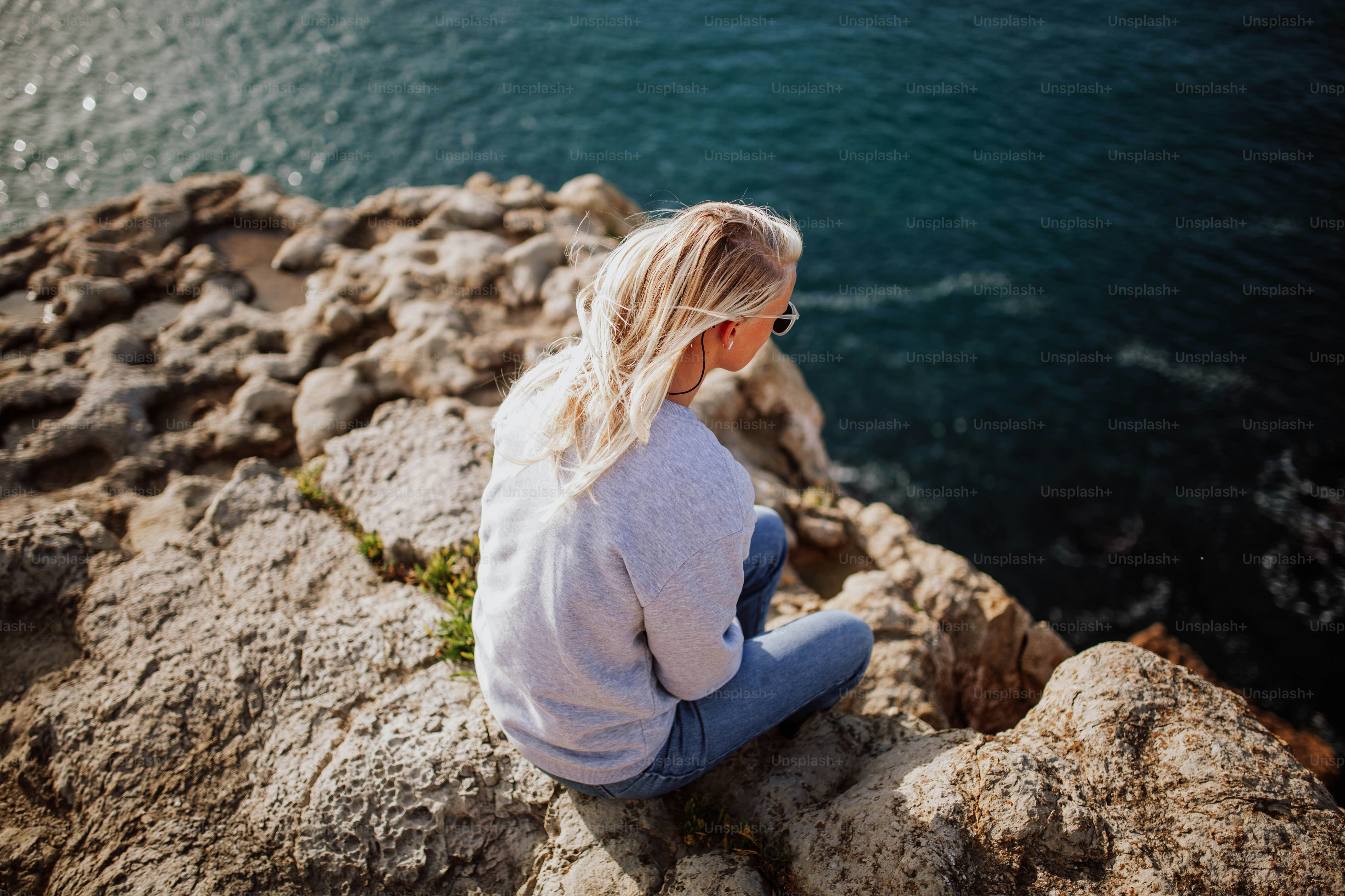 a woman sitting on a rock looking at the water