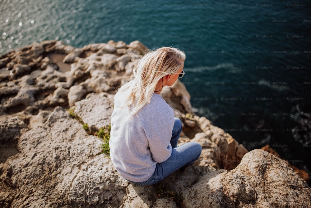 a woman sitting on a rock looking at the water