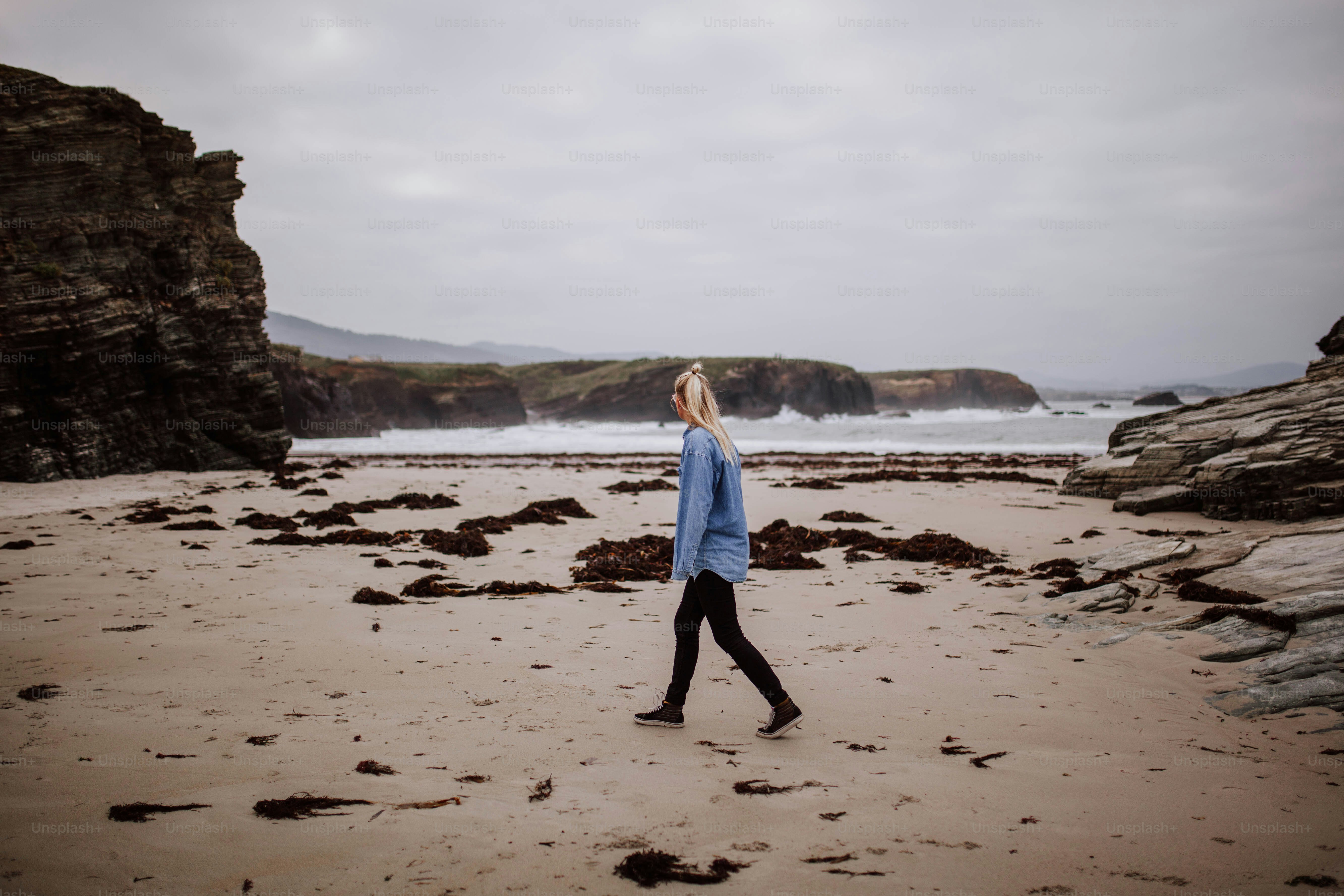 A woman walking on a beach next to the ocean photo – Beach Image on ...