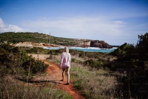 a woman walking down a dirt road next to a body of water