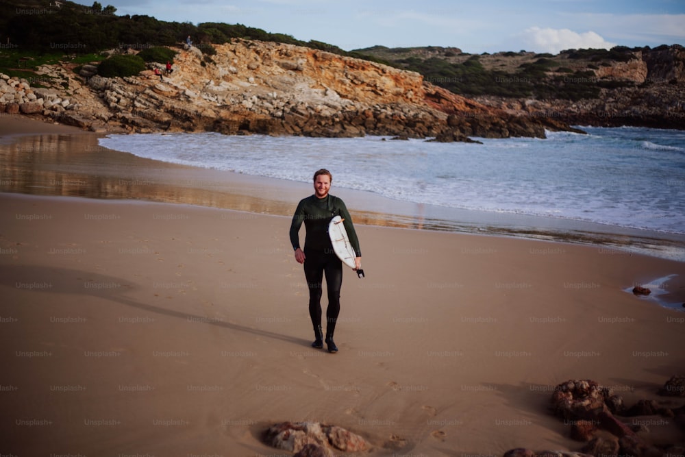 um homem segurando uma prancha de surf em cima de uma praia de areia