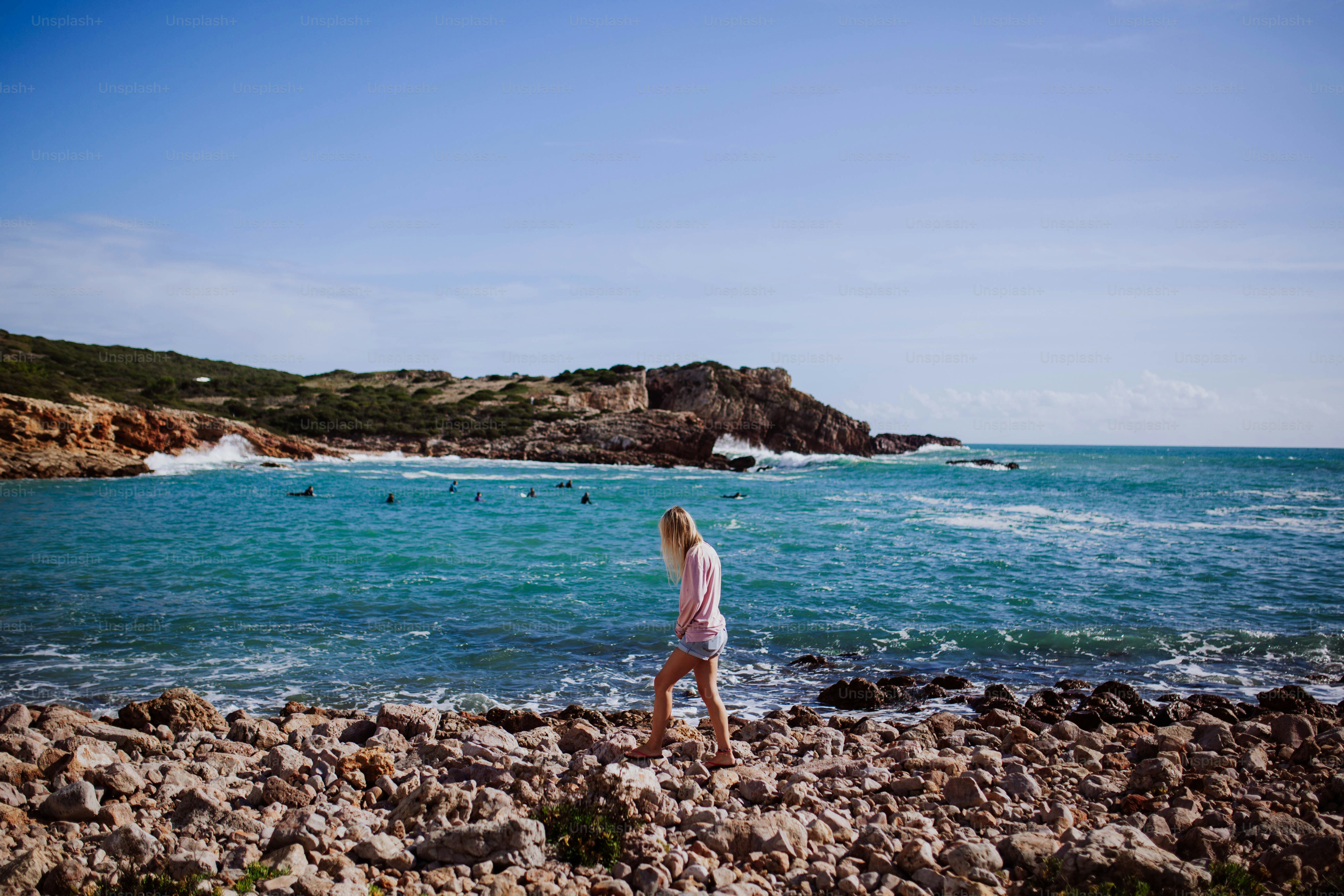 a woman standing on a rocky beach next to the ocean