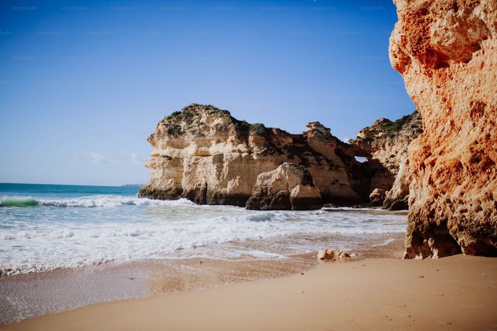 a sandy beach next to a large rock formation