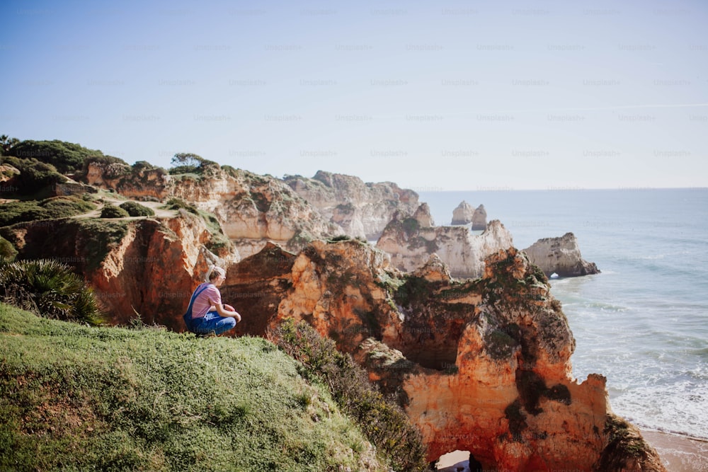 a woman sitting on a cliff overlooking the ocean