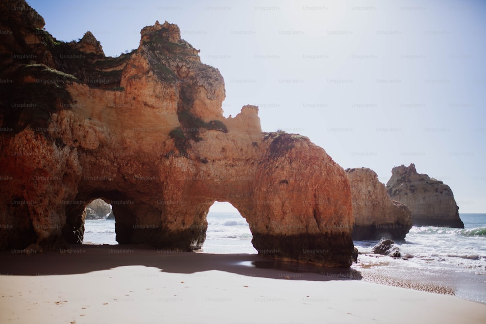 uma grande formação rochosa em uma praia perto do oceano