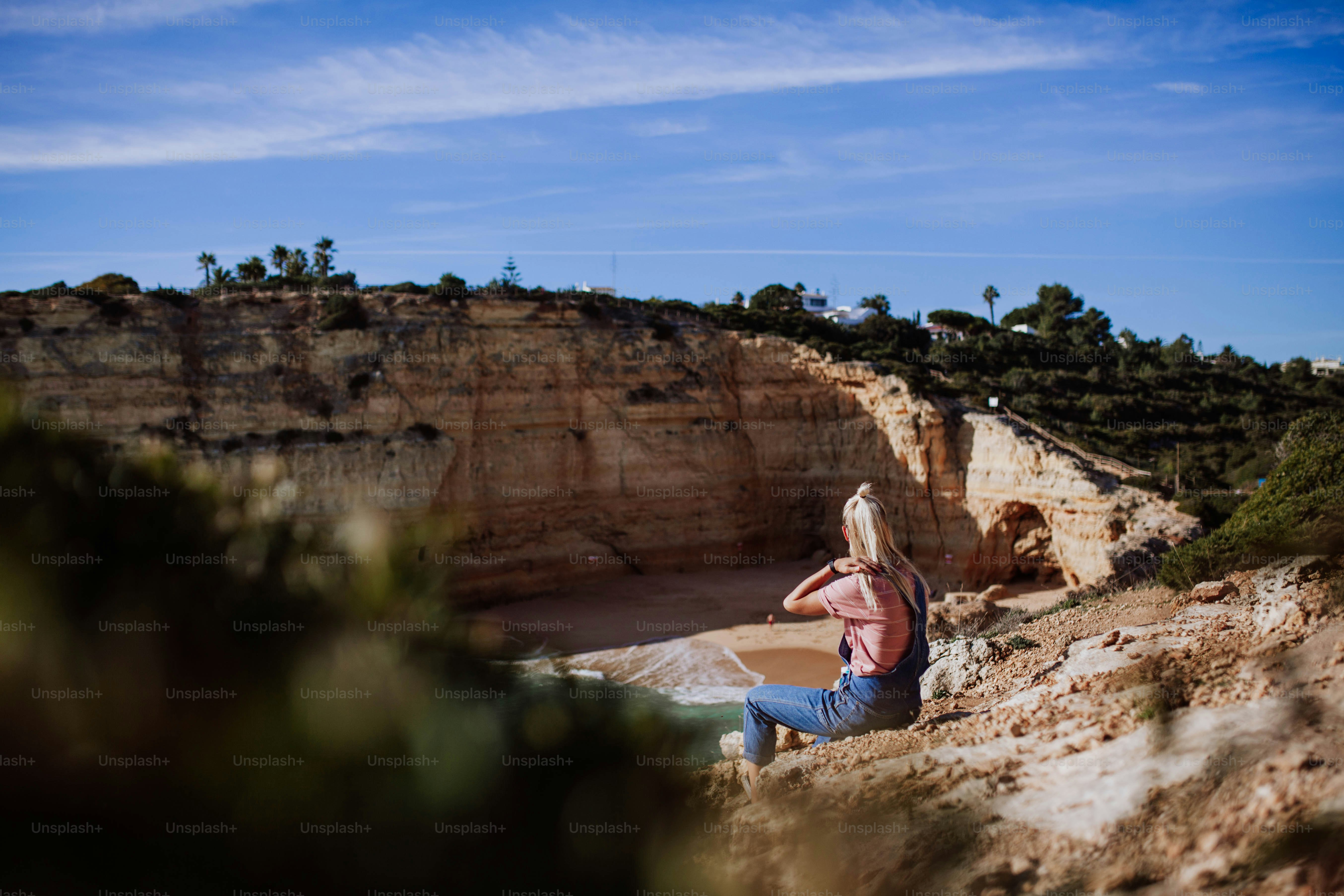 a woman sitting on a cliff overlooking a body of water