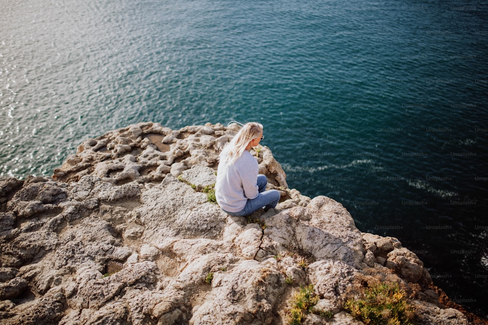 Eine Frau sitzt auf einem Felsen am Meer