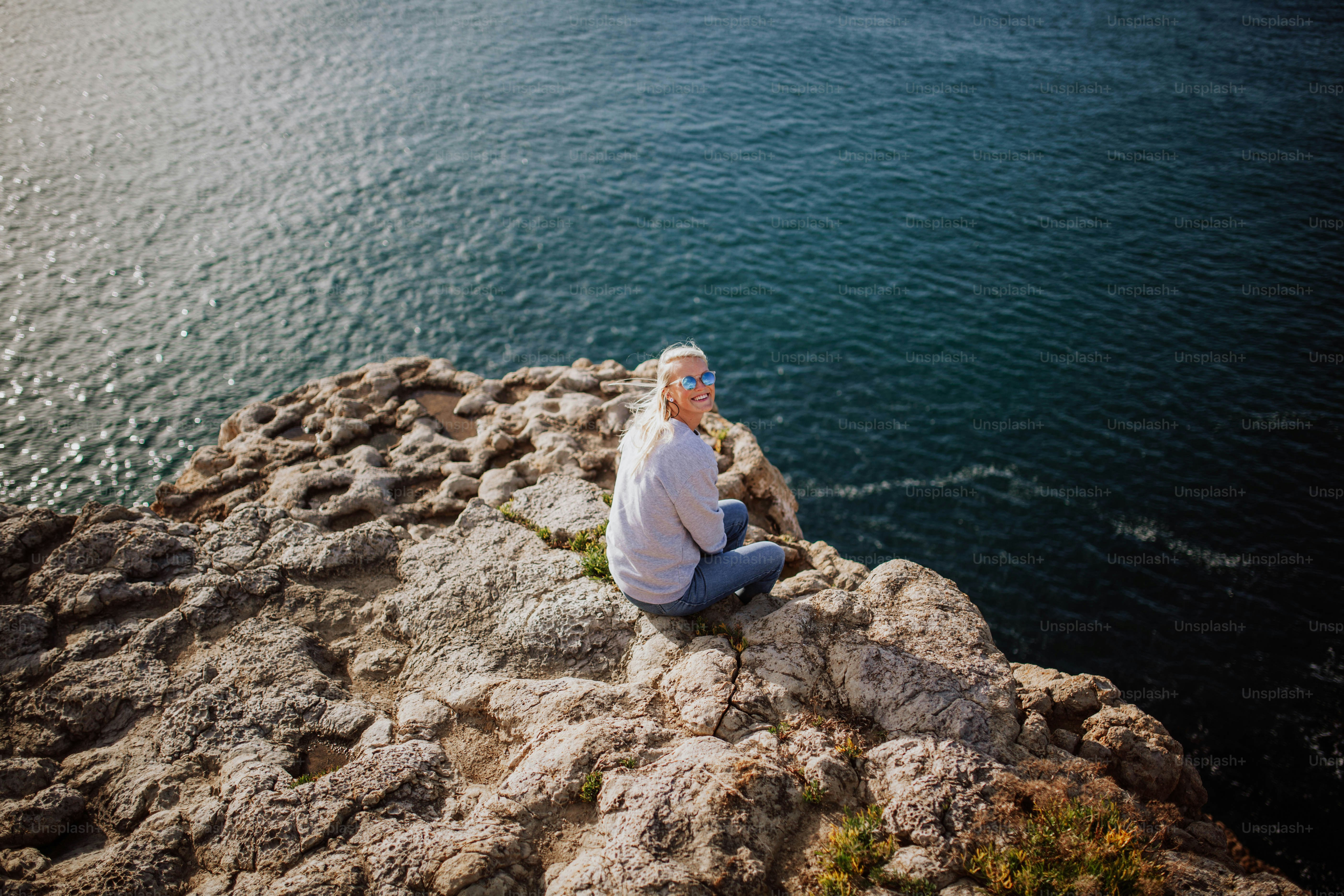 a man sitting on top of a rock next to the ocean