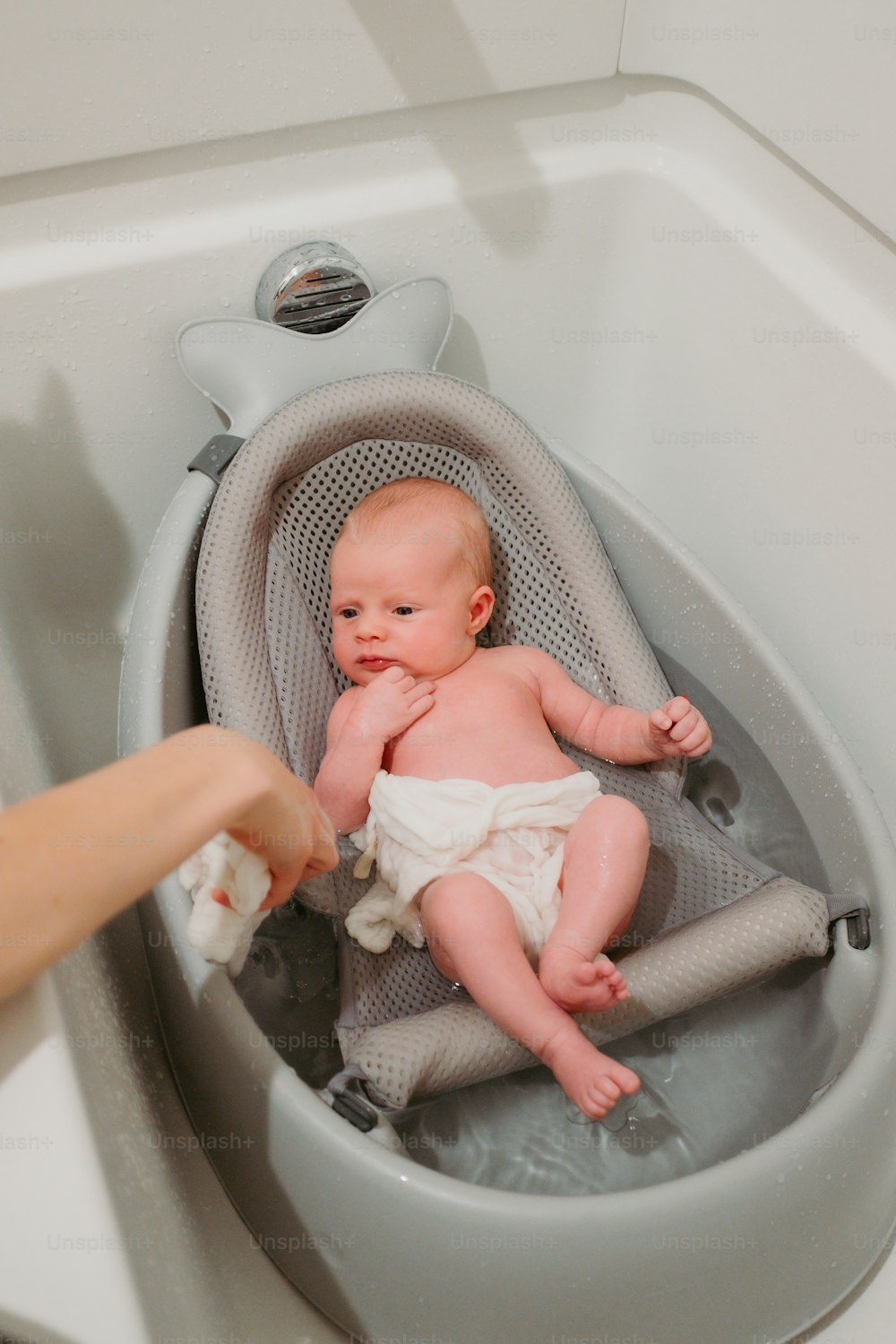 Ein Baby in einer Badewanne, das von einer Person gehalten wird