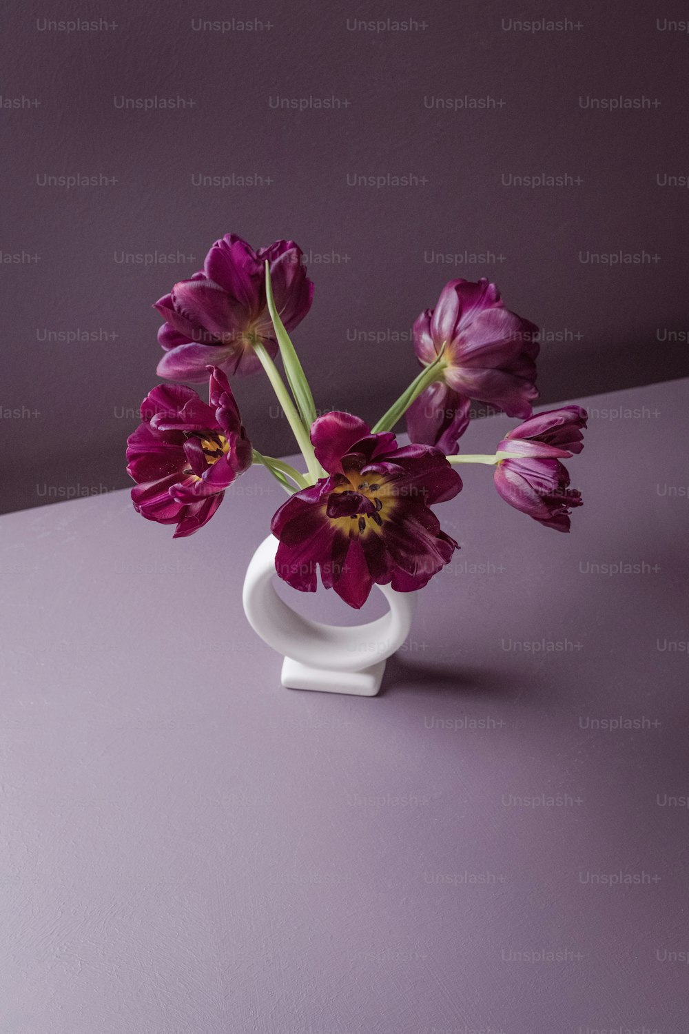 eine weiße Vase gefüllt mit lila Blumen auf einem Tisch