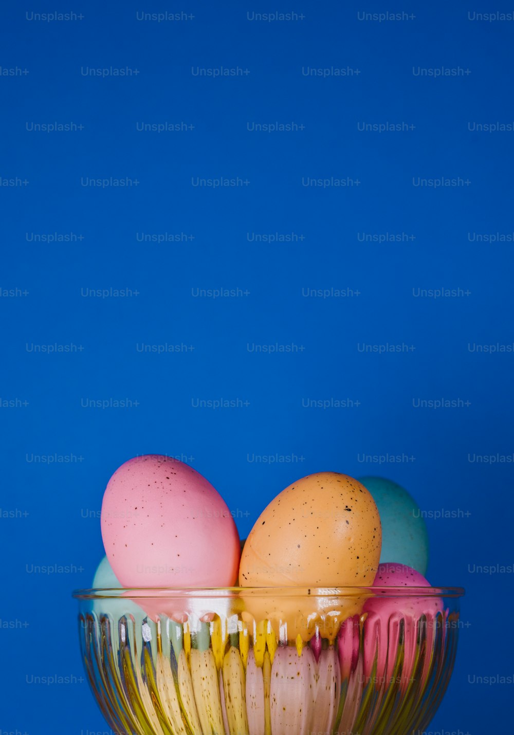 a glass bowl filled with colored eggs on a blue background