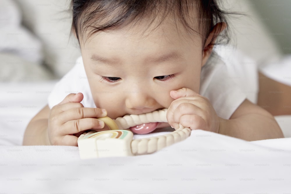 un bebé masticando un teléfono de juguete mientras está acostado en una cama