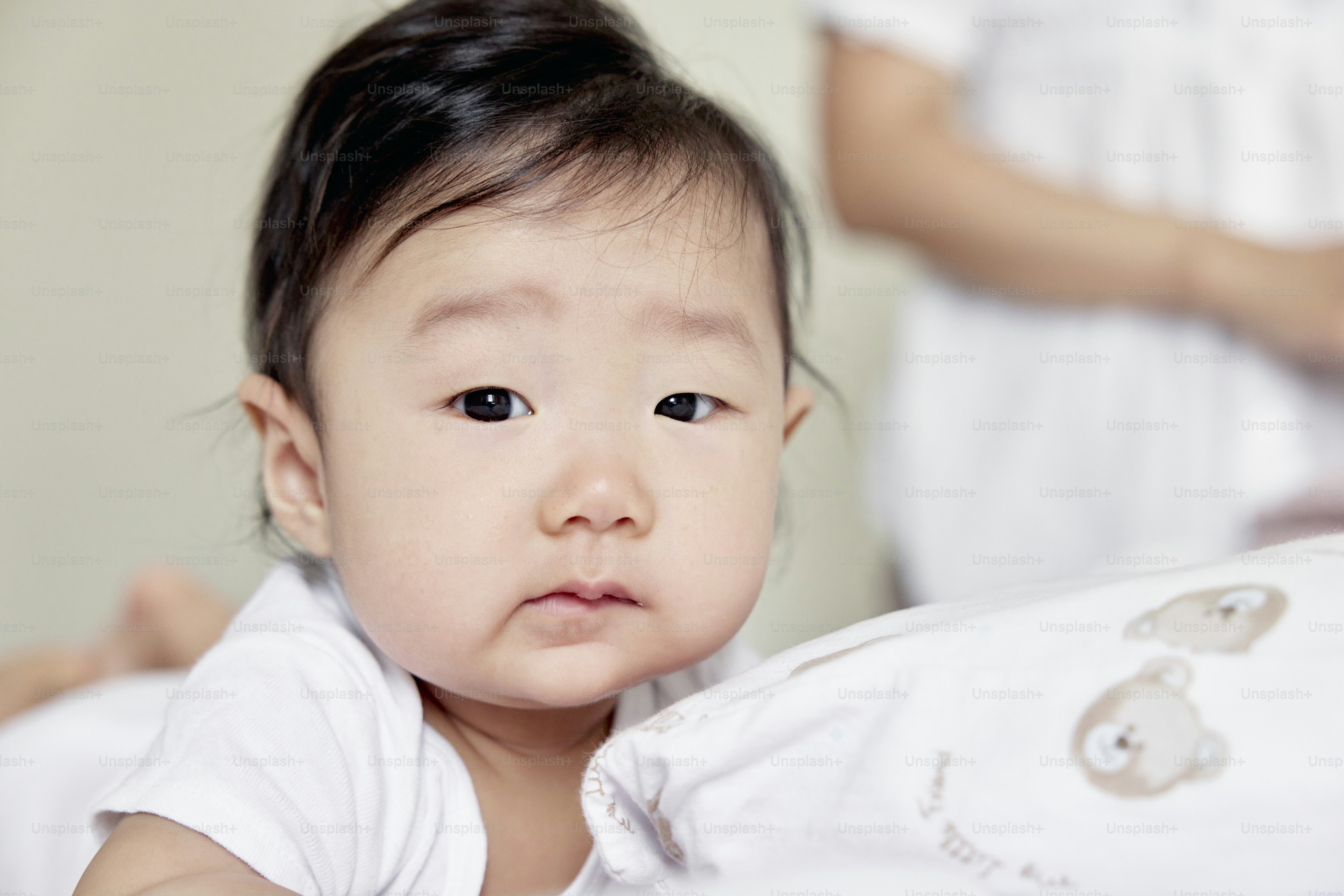 a baby is looking at the camera with a woman in the background
