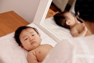 a baby laying on a bed in front of a mirror