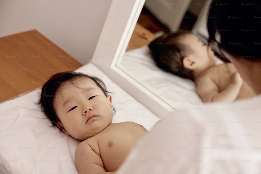 a baby laying on a bed in front of a mirror