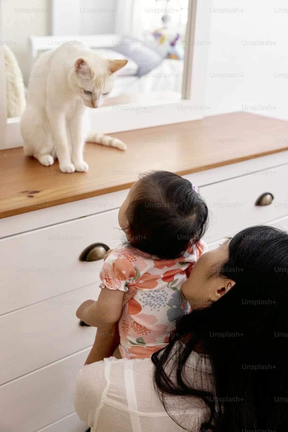 a woman holding a child looking at a cat