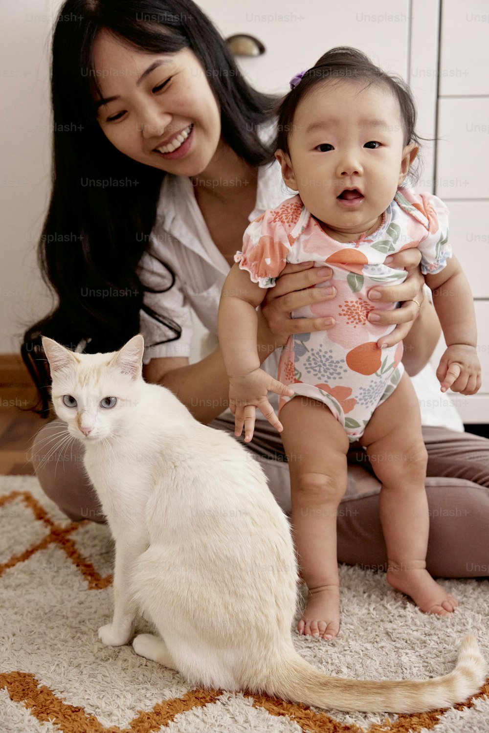 a woman holding a baby and a white cat