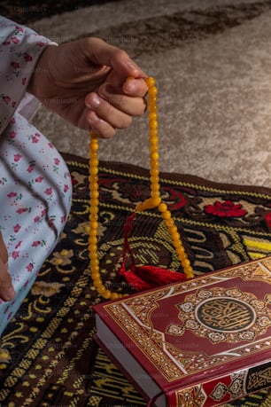 a person holding a beaded rosary next to a book