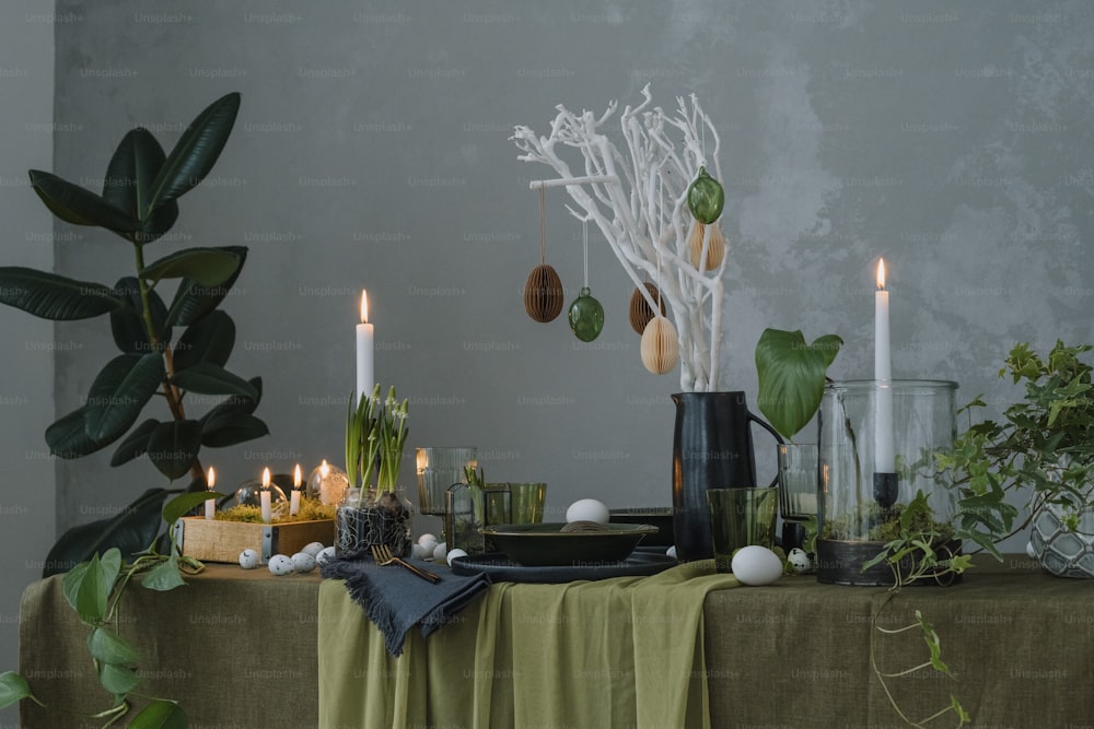 uma mesa coberta com velas e plantas ao lado de uma parede