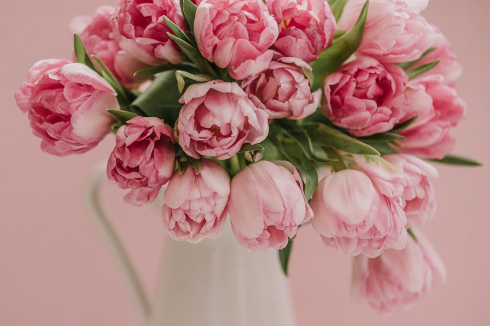 um vaso branco cheio de flores cor-de-rosa em cima de uma mesa