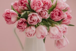 a white vase filled with pink flowers on top of a table