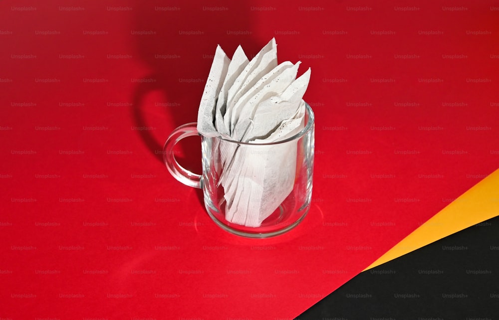 a glass mug filled with white napkins on top of a red and yellow table