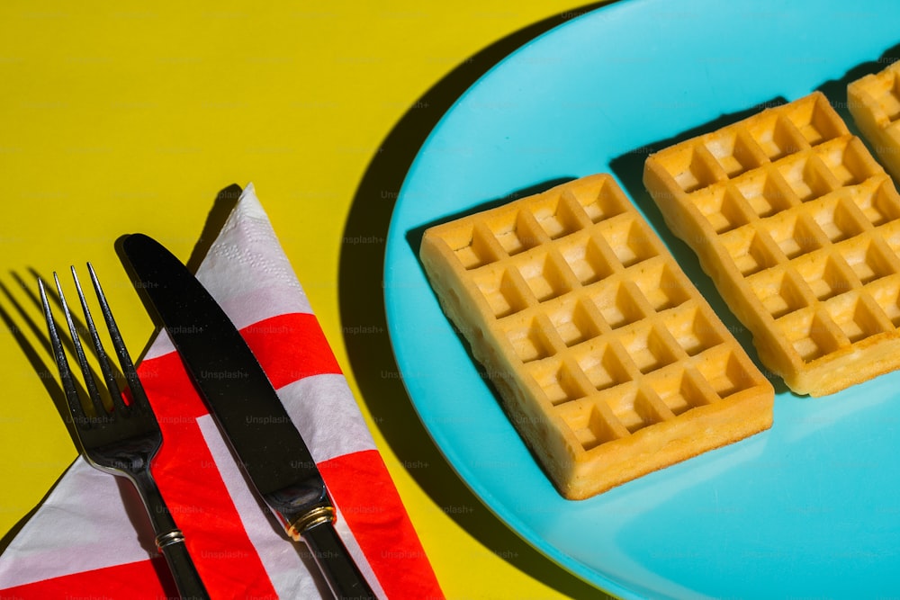 three waffles on a plate next to a fork and knife