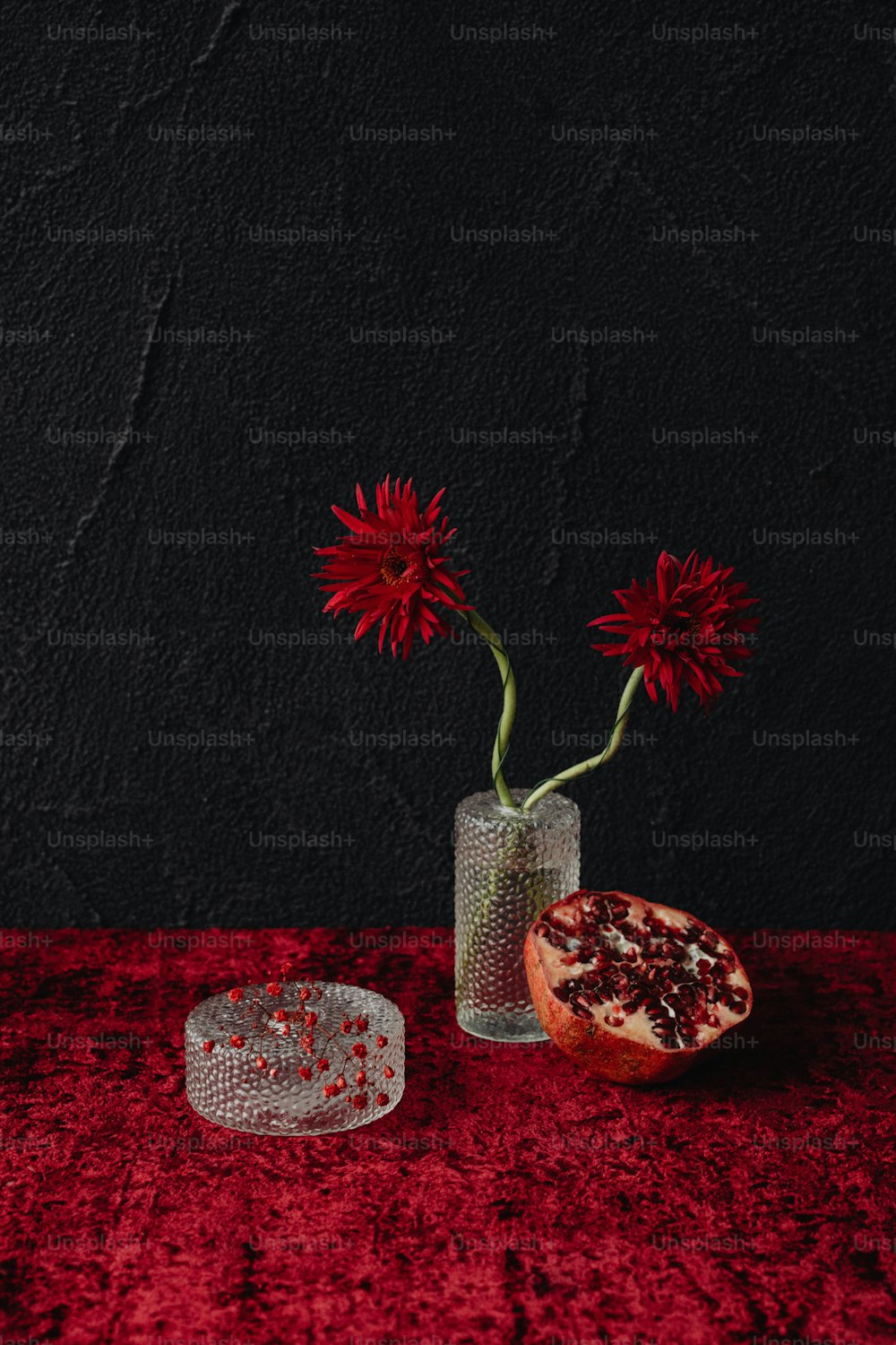 un jarrón de vidrio con una flor y una granada sobre una mesa roja