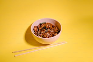 a bowl of noodles with chopsticks on a yellow background