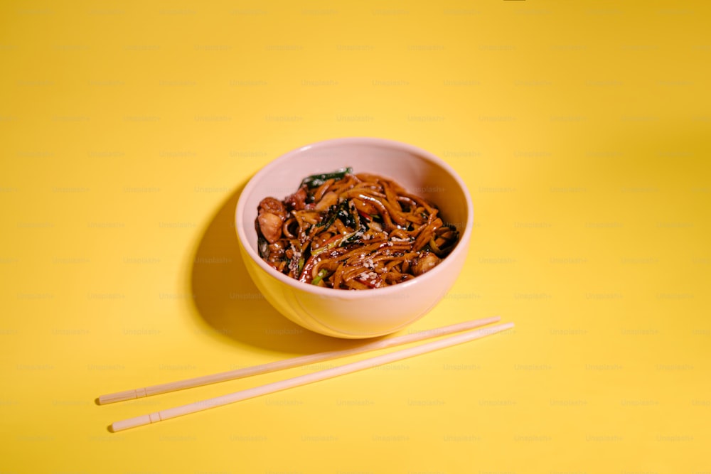 a bowl of noodles with chopsticks on a yellow background