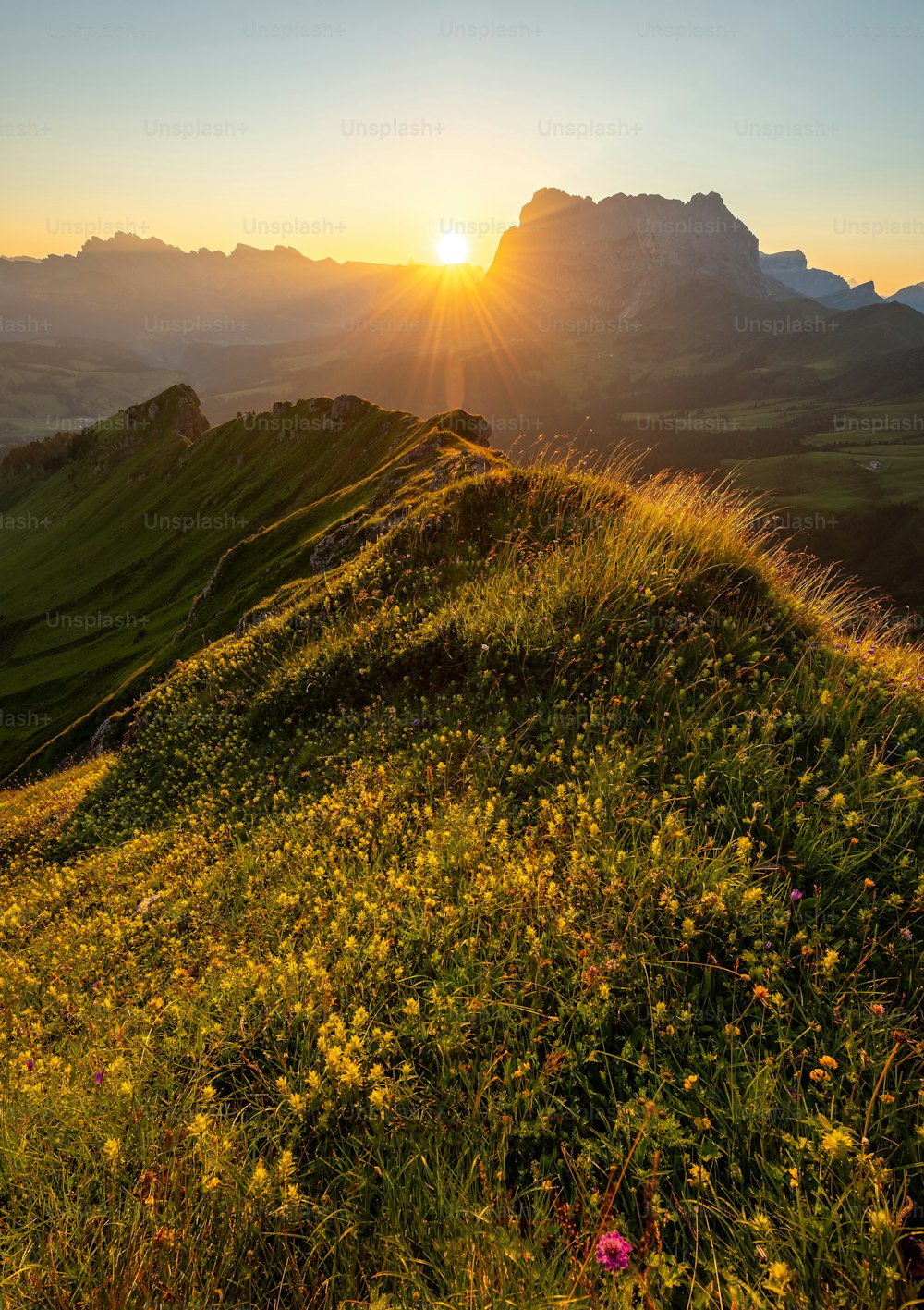 the sun is setting over a grassy hill