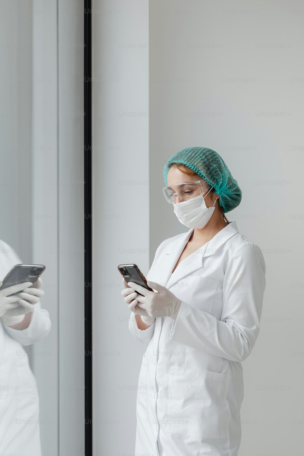 흰색 실험실 코트와 수술용 마스크를 쓴 여성이 휴대폰을 보고 있다