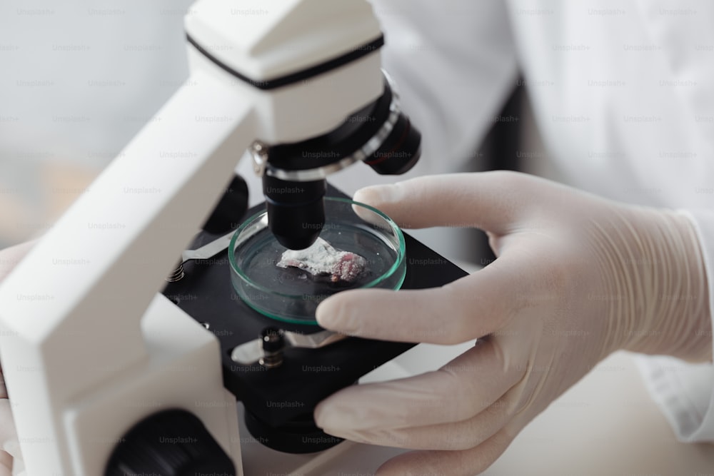 eine Person in weißen Handschuhen, die ein Mikroskop hält