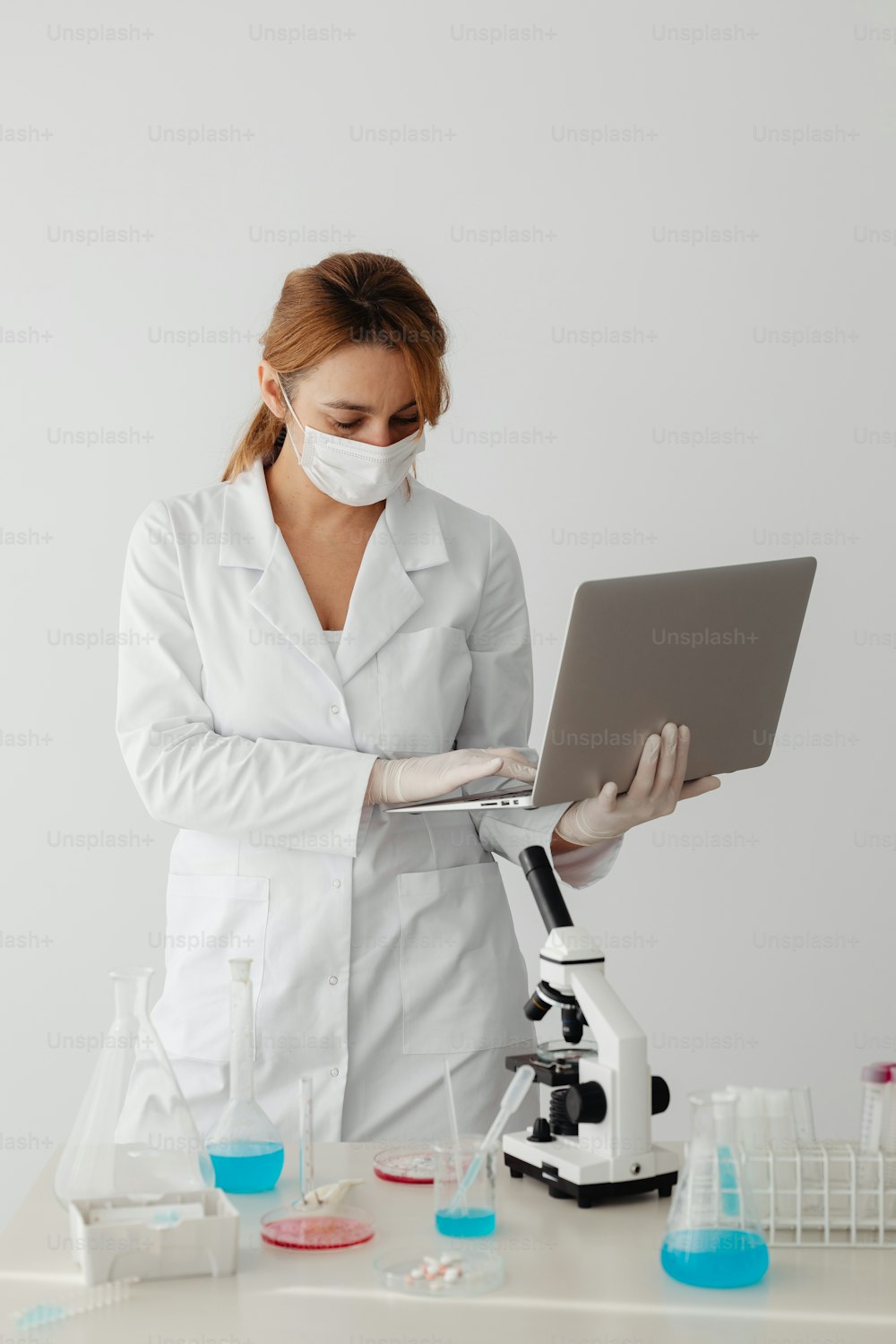 Una mujer con bata blanca de laboratorio usando una computadora portátil