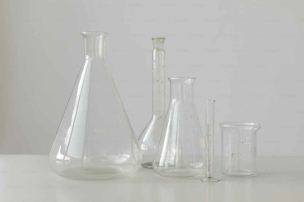una mesa blanca cubierta con tres jarrones de vidrio y una taza medidora