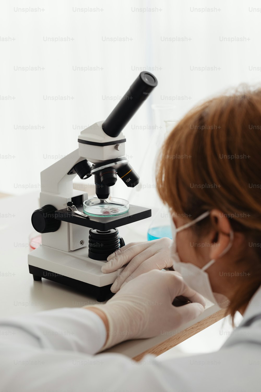 Una mujer con una bata de laboratorio mirando a través de un microscopio