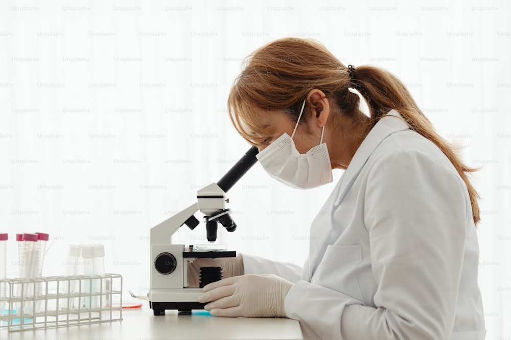 uma mulher em um jaleco branco olhando através de um microscópio