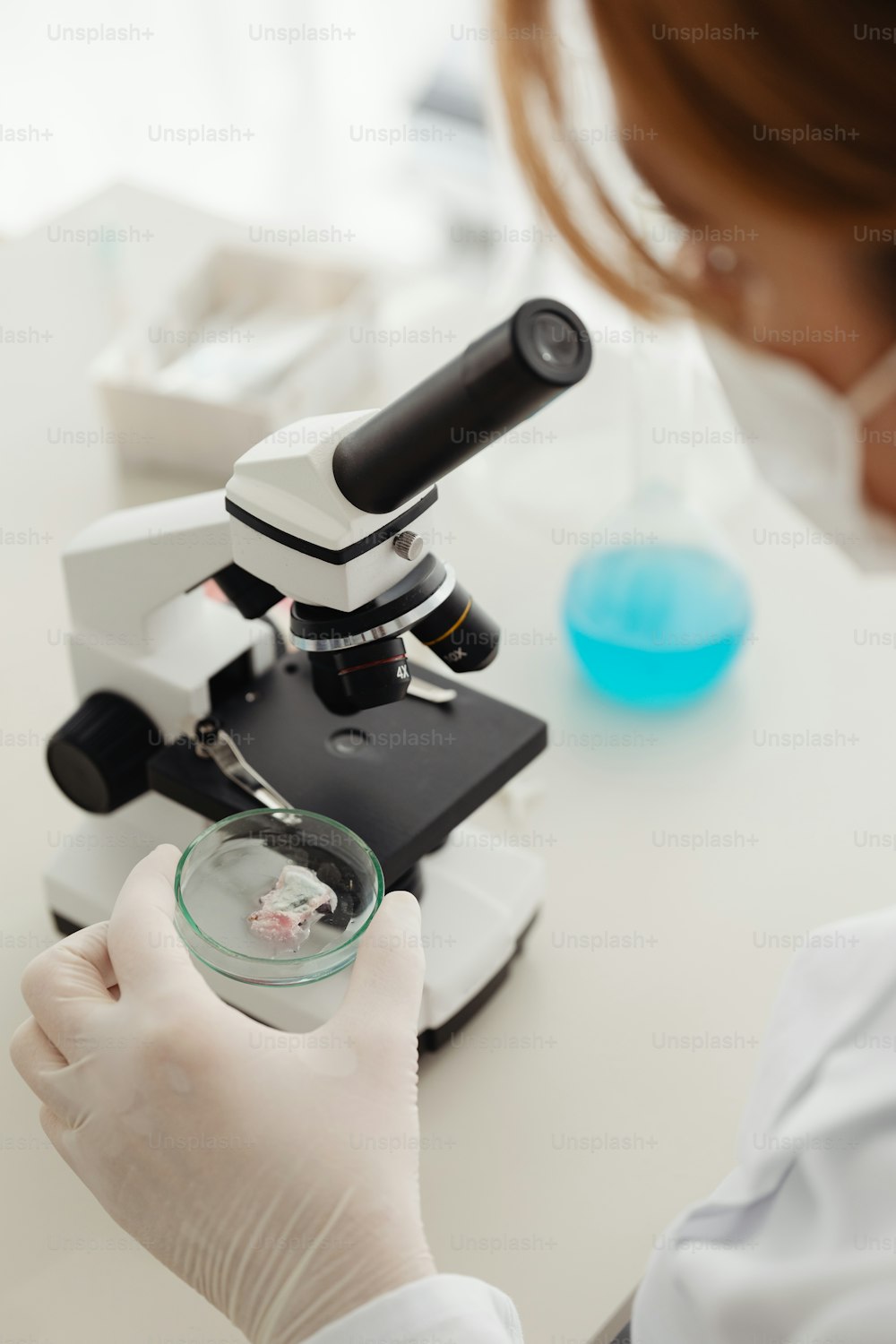 Eine Frau im weißen Laborkittel schaut durch ein Mikroskop