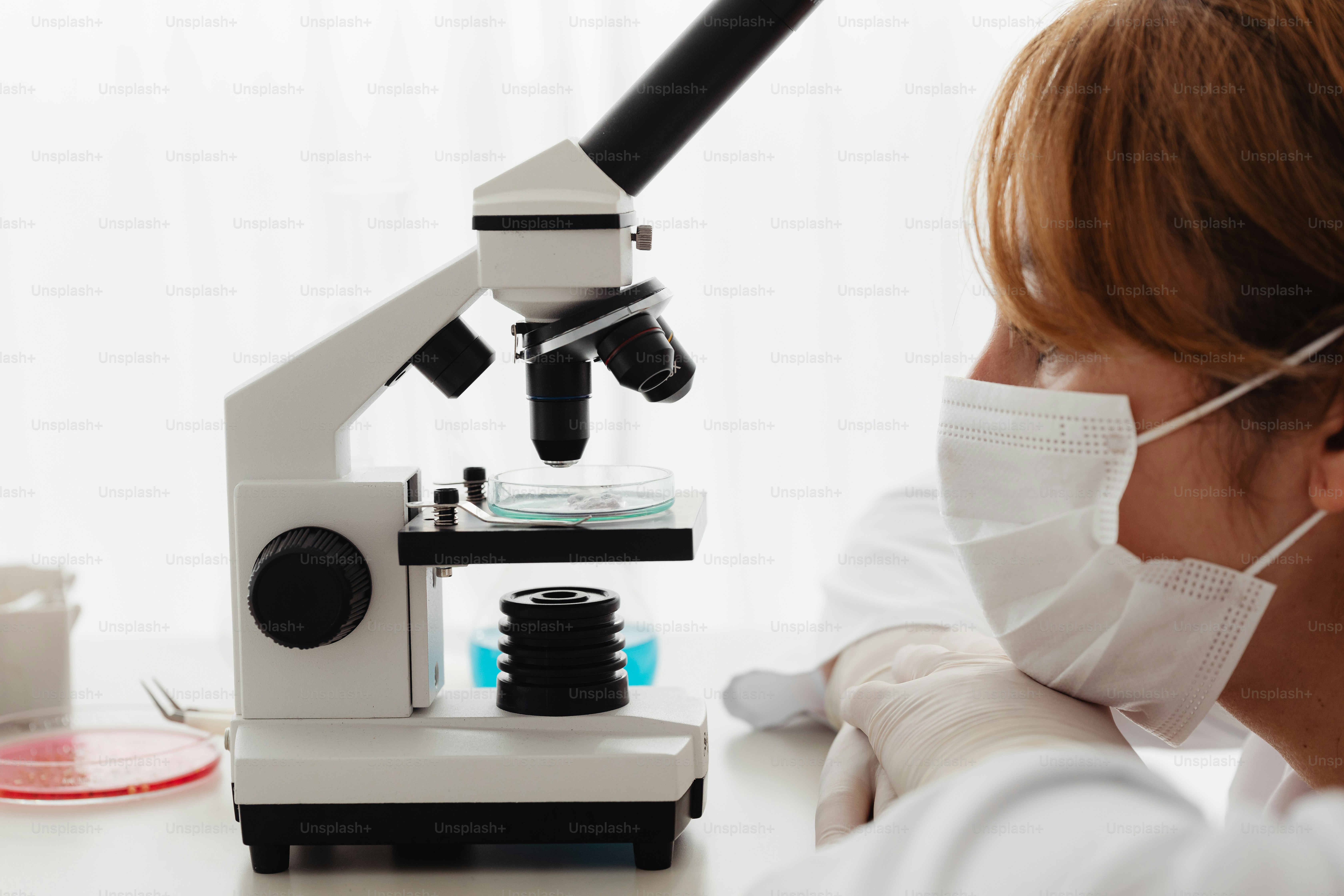Una mujer con una máscara facial mirando a través de un microscopio