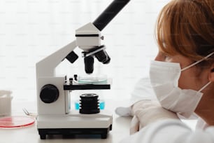 une femme portant un masque facial regardant à travers un microscope