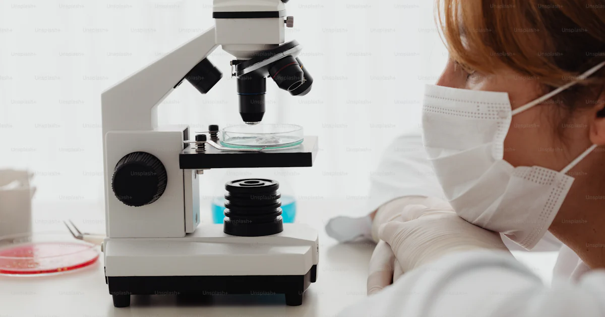 A woman wearing a face mask looking through a microscope photo ...