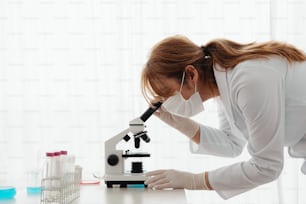 a woman in white lab coat looking through a microscope